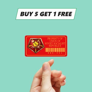 Könnte beinhalten: Ein roter rechteckiger Aufkleber mit goldenem Rand und einem goldenen und roten Emblem. Der Text "PROPERTY OF UNION OF SOVIET SOCIALIST REPUBLICS" ist auf dem Aufkleber aufgedruckt. Der Text "RED-001" ist unten aufgedruckt. Über dem Aufkleber befindet sich ein weißes Banner mit dem Text "BUY 5 GET 1 FREE".