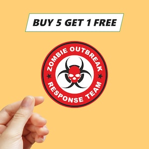 Può includere: Un adesivo rotondo rosso e bianco del Zombie Outbreak Response Team con un simbolo di pericolo biologico e un teschio. Il testo "BUY 5 GET 1 FREE" è visualizzato in un banner verde e bianco.