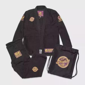 Puede incluir: Un conjunto de uniforme de artes marciales negro, que incluye una chaqueta, pantalones y una bolsa con cordón. La chaqueta y los pantalones tienen parches con logotipos dorados y morados. La bolsa presenta el texto "Shoyoroll".