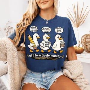 May include: Navy blue t-shirt with a humorous graphic of three ducks with speech bubbles. The ducks have the phrases "Mission: Overthink Everything", "We've Got This... Probably. It's Fine", and "Caffeine. Chaos. Let's Go." The text "off to actively monitor" is also present.
