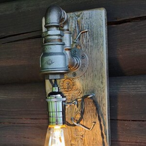 May include: Industrial-style wall sconce featuring a vintage Edison bulb. The fixture is made from metal pipes and fittings, mounted on a weathered wooden board. The bulb emits a warm, inviting glow, perfect for rustic decor.