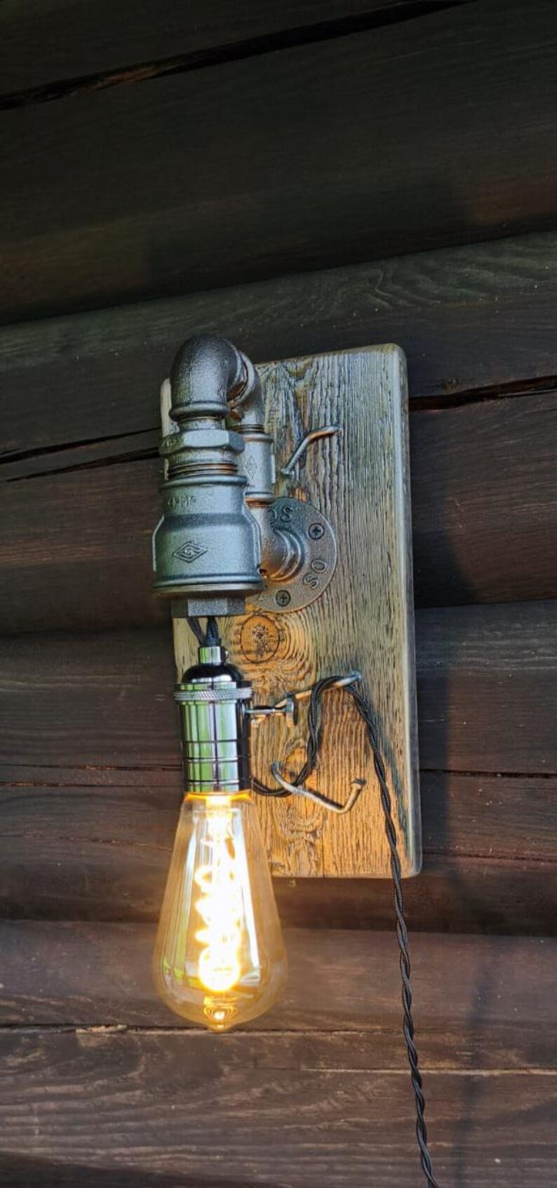 May include: Industrial-style wall sconce featuring a vintage Edison bulb. The fixture is made from metal pipes and fittings, mounted on a weathered wooden board. The bulb emits a warm, inviting glow, perfect for rustic decor.