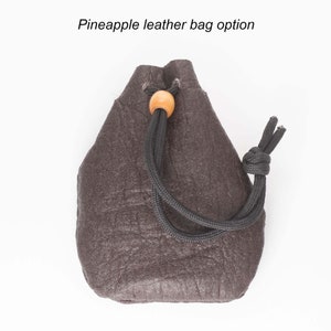 May include: A small, dark brown leather drawstring bag with a wooden toggle. The bag has a textured surface and a black drawstring.