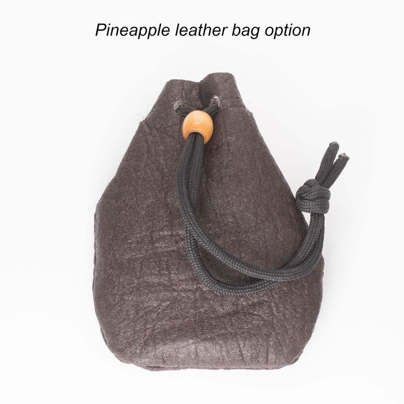 May include: A small, dark brown leather drawstring bag with a wooden toggle. The bag has a textured surface and a black drawstring.