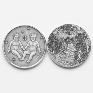 May include: Two silver coins, one with a depiction of the Gemini zodiac sign and the other with a textured surface resembling the moon.