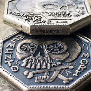 May include: Two silver-toned octagonal coins with skull imagery. The top coin features the text "Memento Vivere" and the bottom coin features the text "Memento Mori".