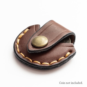 May include: A brown leather coin purse with a snap closure. The purse is stitched with tan thread around the edges. The coin purse is a half-circle shape and has a brass-coloured snap.