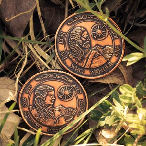 May include: Two round, copper-coloured coins with raised edges and intricate designs. The top coin features a bearded man with long hair and the text "Not All Who Wander Are Lost". The bottom coin features a woman with long hair and the text "All That Is Gold Does Not Glitter".