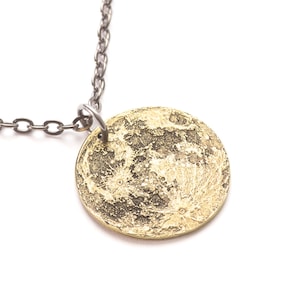 May include: A silver chain necklace with a round brass pendant featuring a detailed image of the moon's surface.