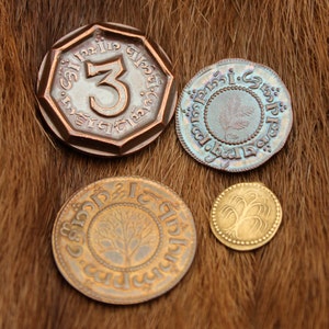 May include: Four Tolkien-themed coins, including a copper coin with the number "3" and the inscription "One Ring to rule them all", a silver coin with a tree design, and two gold coins with tree designs.
