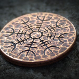 May include: A copper-colored round pendant with a black etched design of a symbol with eight points. The pendant has a textured surface.
