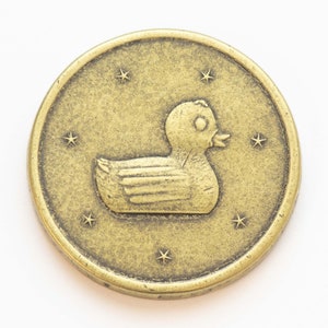 May include: A gold-coloured metal token with a rubber ducky design and five stars around the edge.