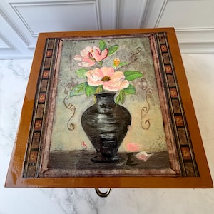 May include: Wooden box with a painted floral design. The artwork features a black vase holding pink flowers with green leaves. The box has a decorative border and a brass pull.