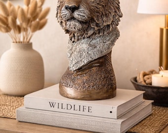 May include: A detailed sculpture of a lion's head with green eyes, resting on a stack of books. The books are titled "WILDLIFE". The sculpture is brown and bronze, with a textured finish. The overall theme is home decor.