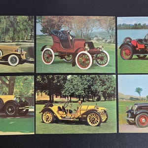 May include: Six vintage car postcards. The postcards feature classic cars in various colors, including tan, red, and yellow. The cars are set against backgrounds of trees, grass, and water. The postcards are arranged in two rows of three.