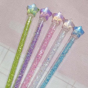 May include: Five colorful star-topped wands. Each wand has a clear tube filled with glitter in shades of green, purple, pink, white, and blue. The star tops have a shimmering, iridescent finish.