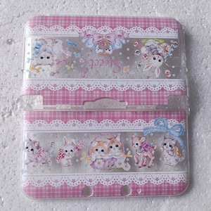 Puede incluir: Una funda rosa y blanca estampada con una parte superior transparente, con ilustraciones de gatitos, conejitos y ciervos. La funda tiene un diseño de encaje y la palabra "Sweet" está escrita en la parte superior. La funda está diseñada para un dispositivo de juego portátil.