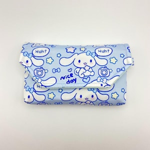 May include: A light blue clutch bag featuring a repeating pattern of a cartoon bunny, cameras, stars, and the text "Huh?" and "Nice day". The bag is folded over and has a white interior.
