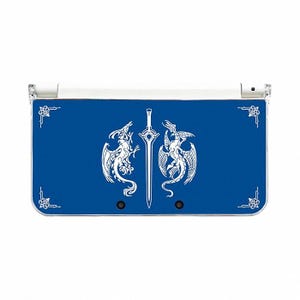 May include: A blue Nintendo 3DS console skin featuring a white design of two dragons flanking a sword. The skin has decorative corner elements and is designed to fit the console's dimensions.