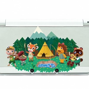 Op de afbeelding: Witte Nintendo 3DS XL-console met een kleurrijk kampeertafereel. De afbeelding toont stripfiguren, een tent en een grill, tegen een achtergrond van bergen en bomen, wat een speels buitenthema creëert.