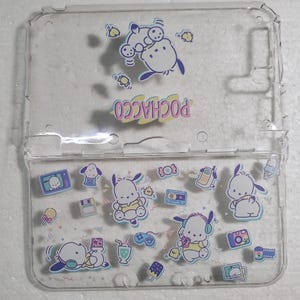 May include: A clear plastic case for a Nintendo Switch featuring a Pochacco design. The case is decorated with various Pochacco characters and images, including a Pochacco wearing a yellow shirt and headphones, a Pochacco wearing a yellow shirt and a chick, a Pochacco wearing a yellow shirt and a lollipop, and a Pochacco wearing a yellow shirt and a cassette tape.