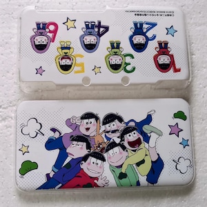 Könnte beinhalten: Zwei weiße Nintendo 3DS-Hüllen. Eine Hülle zeigt Zeichentrickfiguren mit Zahlen und Sternen. Die andere Hülle hat eine Gruppe von Zeichentrickfiguren. Die Hüllen bestehen aus transparentem Kunststoff.