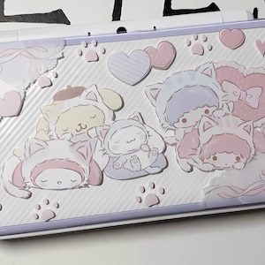 Puede incluir: Una funda para Nintendo Switch de color lila claro y blanco con personajes de gatos de dibujos animados en varias poses. La funda tiene una superficie texturizada con huellas de patas, corazones y lazos. Los personajes de gatos son de colores pastel.