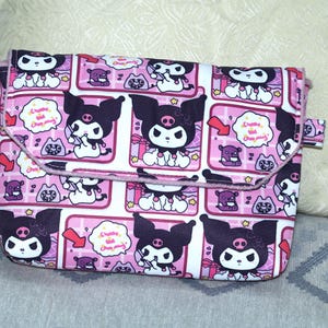 May include: A rectangular crossbody bag featuring a repeating pattern of the character Kuromi on a pink and white grid background. The design includes small speech bubbles with the text "Create the Charming" and various small icons.