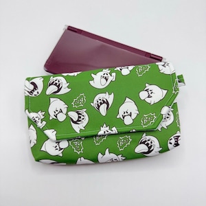May include: Green clutch with a white ghost pattern and a maroon handheld gaming device. The clutch features a flap closure and a repeating design of cartoon ghosts with the word "Boo" in speech bubbles.