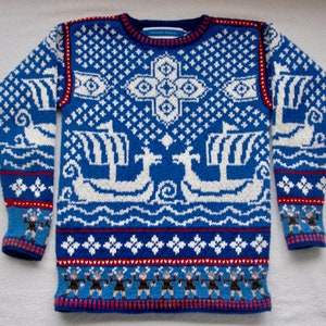 Könnte beinhalten: Ein blauer Strickpullover mit einem weißen und roten Muster mit Schiffen und einem Kreuz. Der Pullover hat einen Rundhalsausschnitt und lange Ärmel.