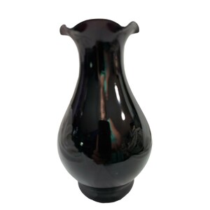 May include: A glossy black vase with a ruffled rim. The vase has a bulbous body and a flared opening. The surface reflects light, and subtle embossed floral patterns are visible on the lower portion.