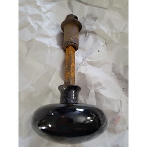 May include: A black ceramic door knob with a rusty metal spindle and a metal cap on the top.