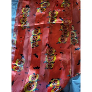 May include: A Halloween-themed table runner with a repeating pattern of stacked jack-o'-lanterns and black bats on a red background with vertical stripes. The pumpkins are yellow and orange with carved faces.