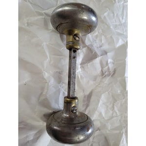 May include: A vintage door knob with a silver finish and brass accents. The knob is in the shape of a sphere and has a long, straight shaft.