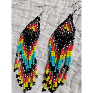 May include: A pair of beaded earrings with a vibrant, colorful design. The earrings feature a black triangular top with red, yellow, and silver accents. Long beaded strands in turquoise, red, and yellow hang from the bottom, creating a striking visual effect.