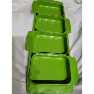 May include: A set of four bright green rectangular serving trays with rounded corners and integrated handles. The trays are stacked on a larger, matching green base tray, creating a tiered presentation. The trays are made of a glossy material.