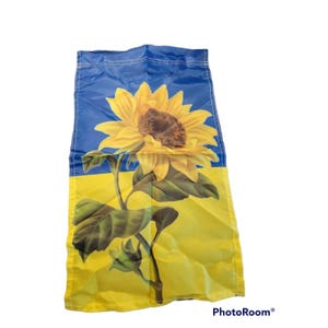 May include: A rectangular fabric garden flag featuring a horizontal blue and yellow color block design. A large, detailed yellow sunflower with a brown center and green leaves is printed in the center, spanning across both color sections.