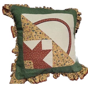 May include: Square decorative pillow with a patchwork design. The pillow features a central design of a leaf and a curved line in shades of red, white, and tan, surrounded by a green border and ruffled edges. The pillow is approximately 16 inches square.