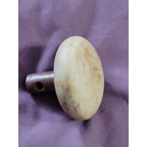May include: A white marble door knob with a brown wooden stem. The knob has a mottled appearance and a hole in the stem.