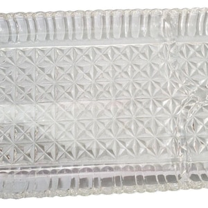 May include: A clear glass rectangular serving tray with a diamond pattern in the center and a ribbed border. The tray has handles on each end. This vintage tray is perfect for serving appetizers or desserts.