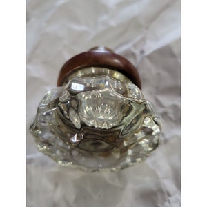 May include: A clear glass door knob with a faceted design and a brown wooden base.