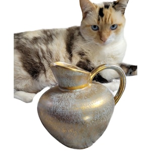 May include: A gold and white ceramic pitcher with a speckled glaze. The pitcher has a wide mouth and a handle.