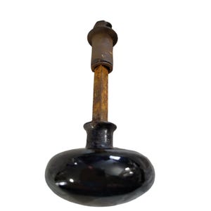 May include: A black ceramic door knob with a metal spindle and a metal cap on the top. The knob is oval shaped and has a shiny finish.