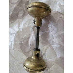 May include: A brass door knob with a round, domed top and a long, straight shaft. The knob is in a worn, antique condition.
