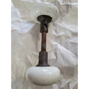May include: A vintage white porcelain door knob with a metal spindle and a rusty finish.