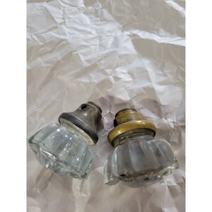 May include: Two vintage glass door knobs with metal bases. One knob has a brass base and the other has a silver base.