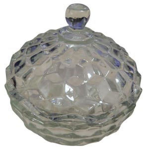 May include: A clear glass candy dish with a faceted, diamond-like pattern. The dish has a matching lid with a small, round knob. The glass has a slight blue tint, and the dish is designed to hold small items.
