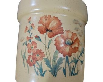 Könnte beinhalten: Ein zylindrischer Keramikbehälter mit cremefarbener, gesprenkelter Oberfläche, der mit einer botanischen Illustration von großen orange-roten Mohnblumen und kleineren, zarten Wildblumen mit grünen Stängeln und Blättern auf der Vorderseite bedruckt ist.