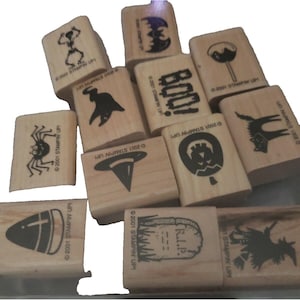May include: A collection of wooden Halloween-themed stamps. The stamps feature various spooky designs, including a skeleton, bat, ghost, spider, witch hat, and jack-o'-lantern. The word "BOO!" is also featured. Each stamp is marked with "©2001 STAMPIN' UP!"