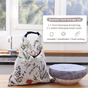 May include: A beeswax food storage set featuring a linen bread bag and a cotton bowl cover. The bag and cover are white with a floral pattern in shades of purple, green, and red. The text on the image says the set is reusable, breathable, and fresh-locking.